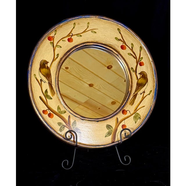 This is a decorative round wall mirror featuring a hand-painted rim with motifs of birds perched on berry-laden branches....