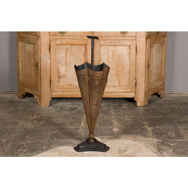 An English brass umbrella stand from circa 1920-1930 shaped as an umbrella with raised motifs and tripartite base. Step...
