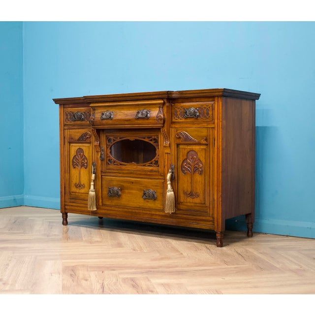 A 1900s Art Nouveau walnut sideboard with carved organic motifs. Two lockable cupboards sit either side of a central...