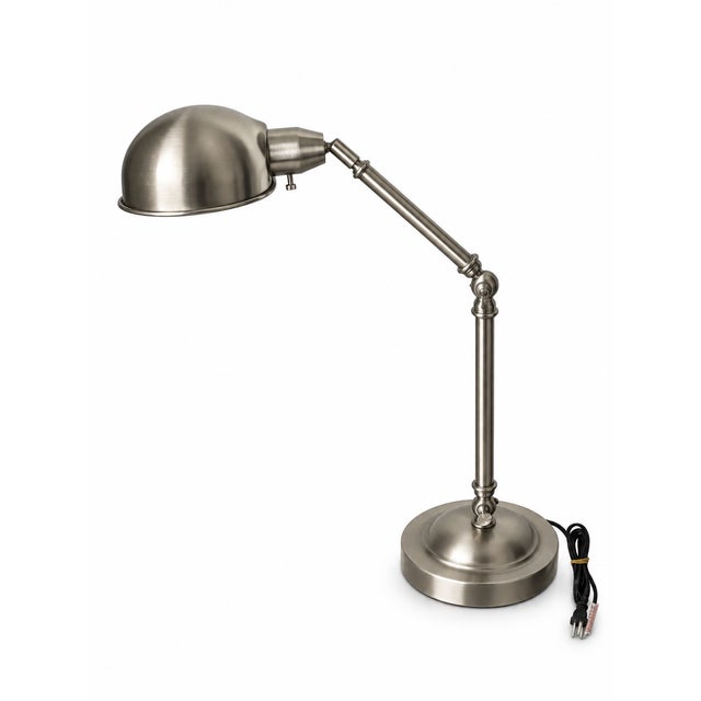 A contemporary industrial-style task lamp featuring a brushed silver-tone metal finish, rounded dome shade, articulated...