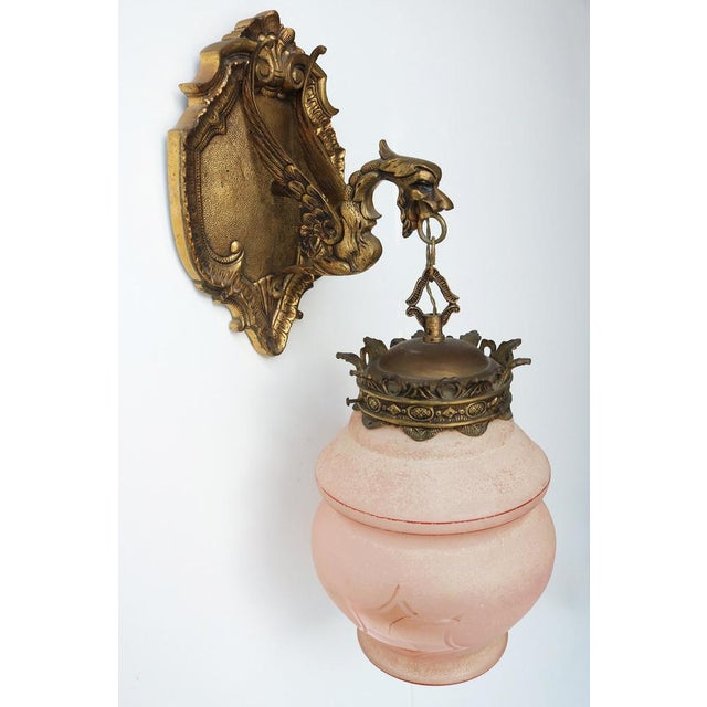 A striking antique gothic revival wall sconce from the early 20th century, featuring a winged dragon or griffin as its...