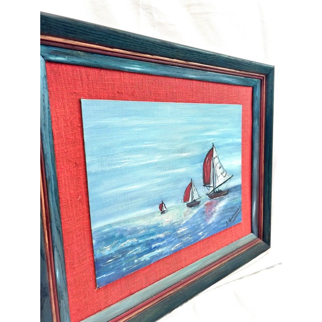A charming 1970s nautical folk art painting depicting sailboats with vibrant red sails gliding across open water. The...