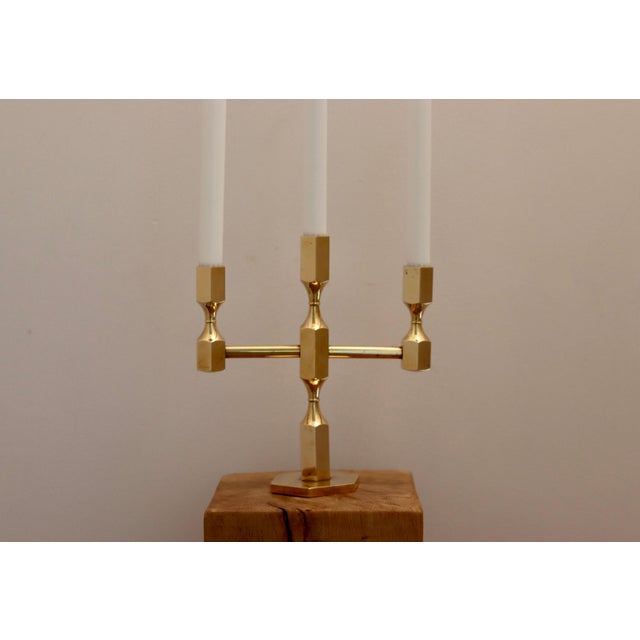 Made in Sweden. This exquisite three-arm candelabra, crafted from solid brass, is a design masterpiece produced by Gusum...