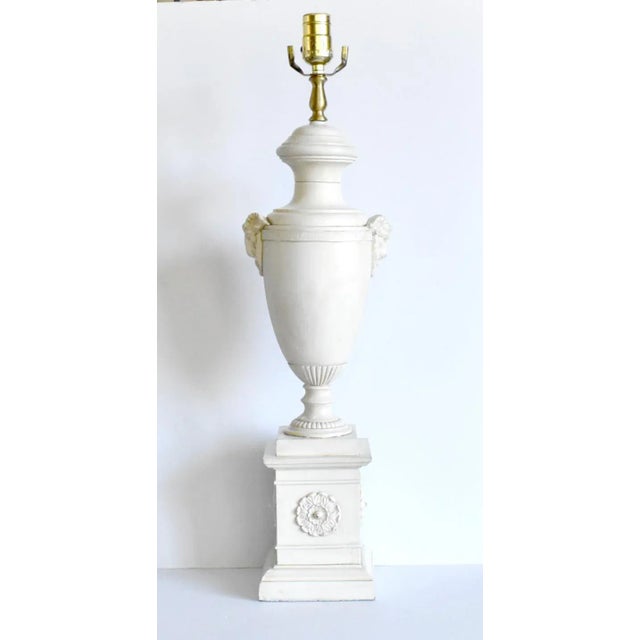 A vintage, mid-century, off-white, neoclassical table lamp with a pedestal urn on a plinth, with ram's head and rosette...