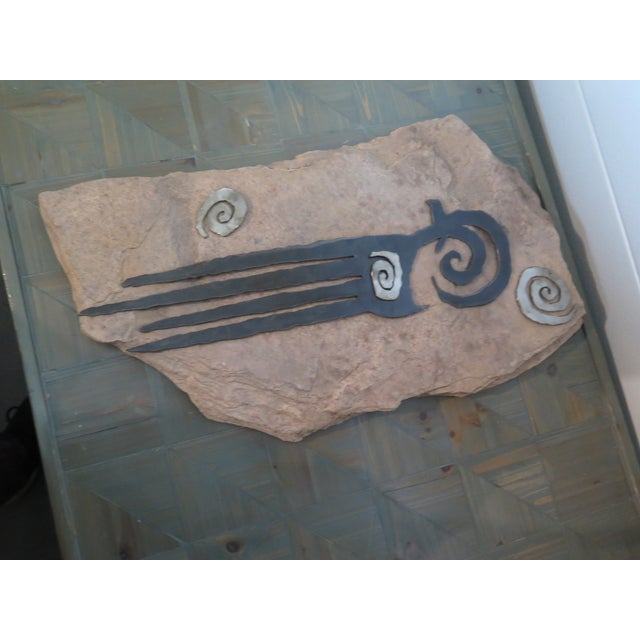 This is a sculptural piece of wall art, featuring a tribal Native American petroglyph-style symbol that is attached to a...
