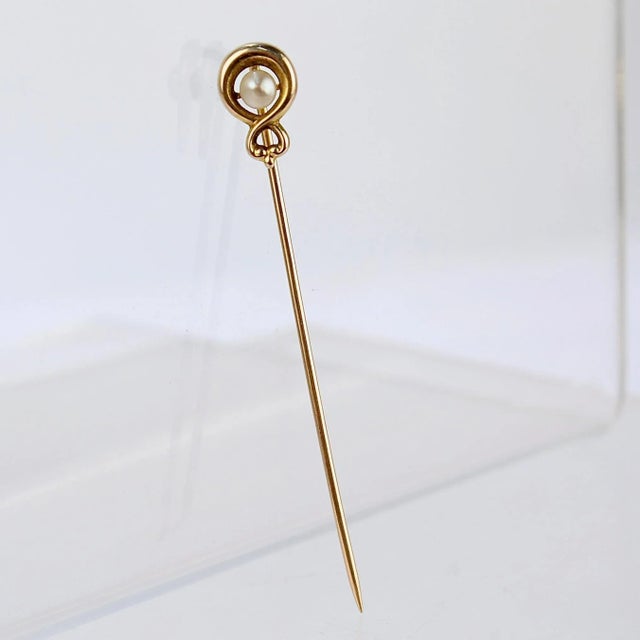 A very fine 10k gold and seed pearl stickpin. With a round white pearl set in center of a 10k gold infinity loop. Simply a...
