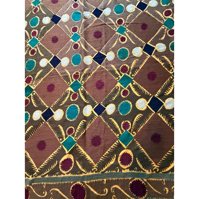 Hand-embroidered Suzani panel from Uzbekistan — a gold lattice over a russet ground, set with teal, navy and ivory...