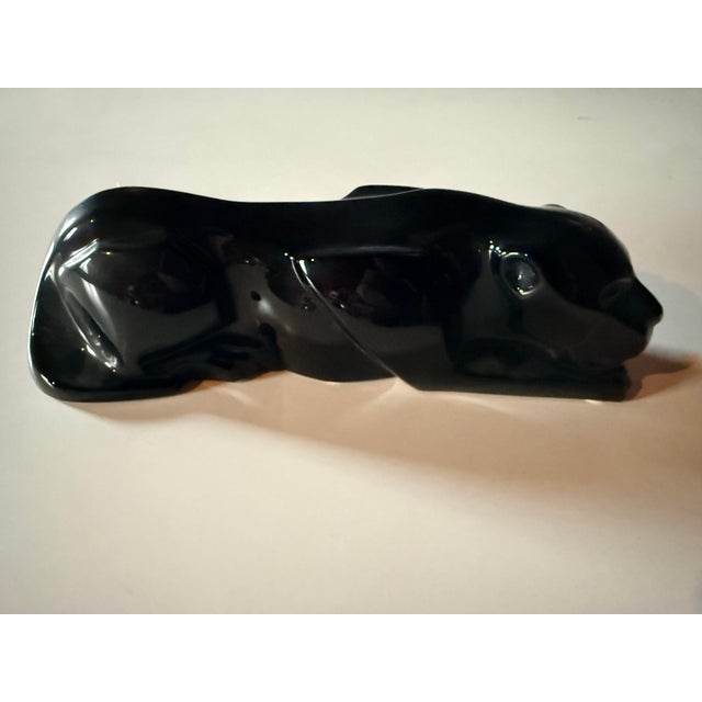 A dramatic Baccarat crouching panther sculpted in deep opaque black crystal, captured mid-stalk in a powerful, low-slung...