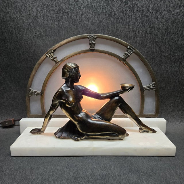 This Art Deco or Egyptian Revival style lamp features a nude woman reclining with a bowl held in her outstretched hand and...