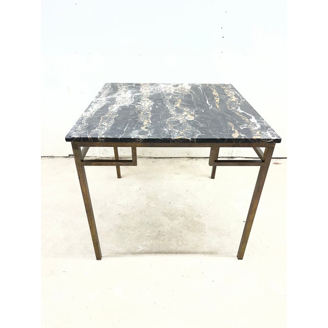 A sophisticated Hollywood Regency dining or game table featuring a richly veined black top supported by an aged brass...