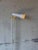 This minimalist floor lamp features an adjustable tubular shade mounted on a slim white metal standard. The sleek...