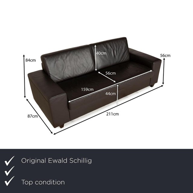 The sofa by Ewald Schillig is upholstered in dark brown leather and rests on slightly tapered wooden legs in a dark shade....