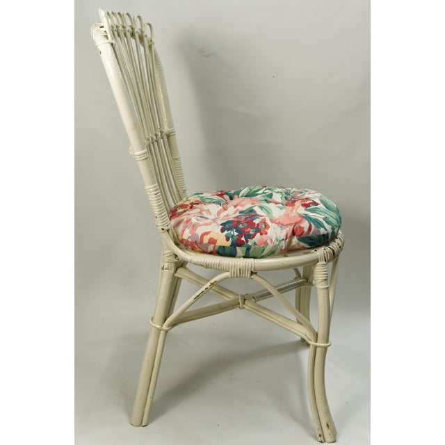 A pair of white wicker accent chairs featuring decorative woven frames and comfortable floral-patterned seat cushions....