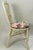 A pair of white wicker accent chairs featuring decorative woven frames and comfortable floral-patterned seat cushions....