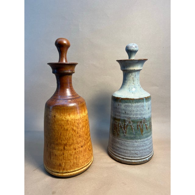 two ceramic bottles with stoppers, showcasing distinct designs and colors. The bottle on the left features a light blue-...
