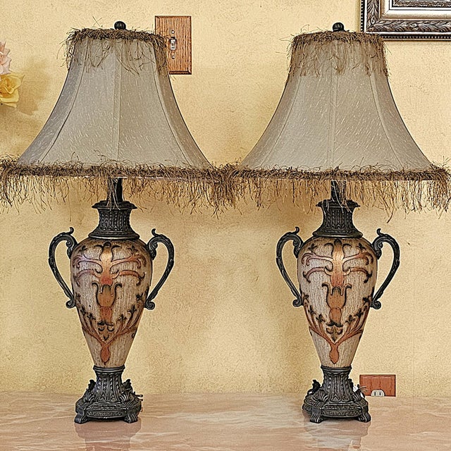 Elegant pair of vintage Neoclassical-style urn table lamps featuring decorative double handles, ornate pedestal bases, and...