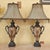 Elegant pair of vintage Neoclassical-style urn table lamps featuring decorative double handles, ornate pedestal bases, and...
