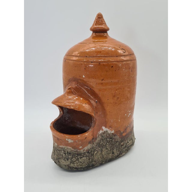 A unique, antique ceramic bird feeder or waterer, shaped like a stylized bird. The object is functional yet features an...