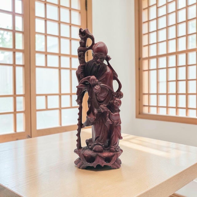 A hand-carved wooden figure depicting Shou Xing, the Chinese God of Longevity, identified by his distinctive high forehead...