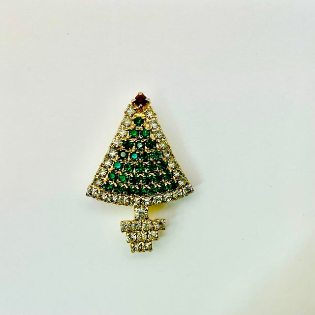 A lovely Christmas Brooch from the 1950s. It features a green rhinestone Christmas tree with a red row of clear...