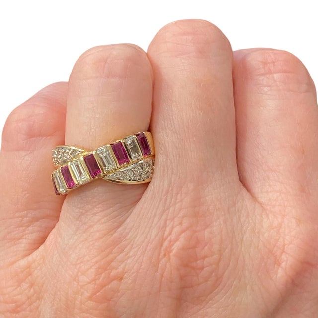 Crafted in 18K yellow gold, the ring showcases a crossover design with alternating baguette-cut rubies and diamonds over...