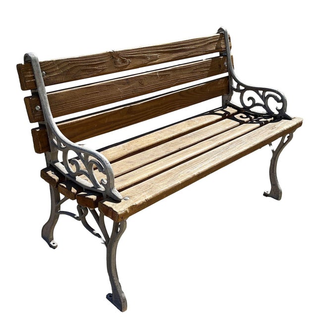 Pair of vintage outdoor benches featuring natural wood slats and elegant cast iron frames with scrolling arm details. The...