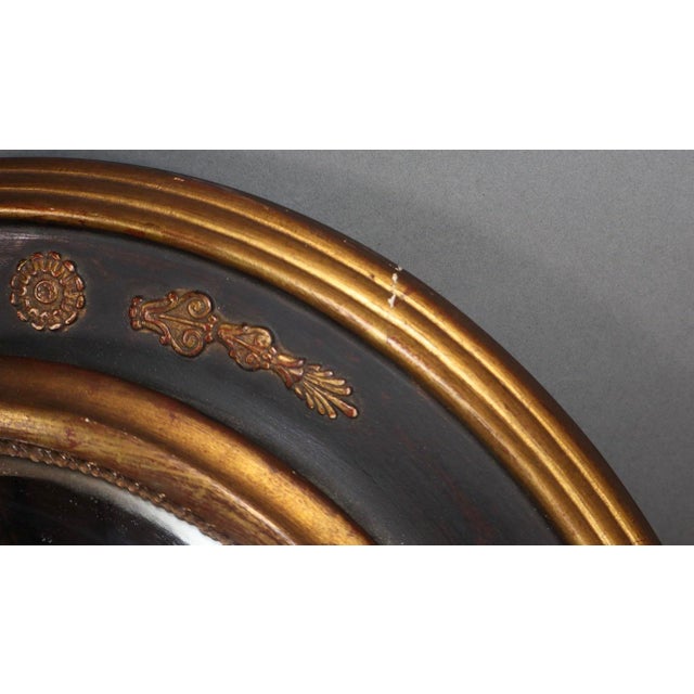 Elegant oval convex butler’s mirror with a black-painted surround enriched by gilt floral and foliate ornament. The deeply...