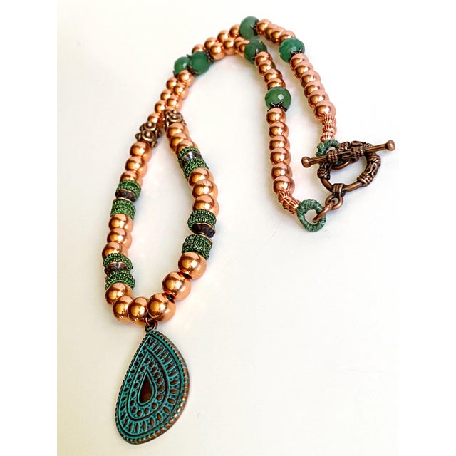 Handcrafted with an artful balance of warm copper and rich green gemstones, this one-of-a-kind statement necklace evokes...