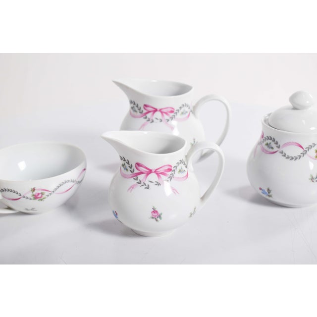 Part of a tea service, in Limoges porcelain. Polychrome decoration with bows and flowers, predominantly pink. Composed of...