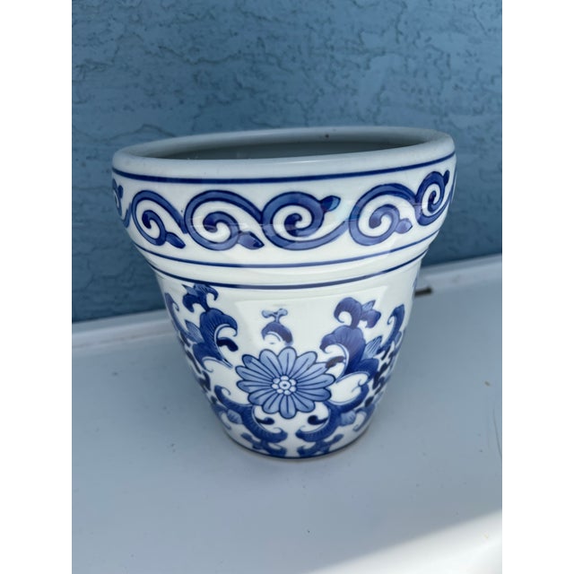 Vintage porcelain Chinoiserie planter features a distinctive blue and white floral motif with a decorative scroll border....