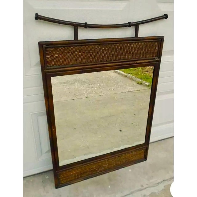 A distinctive vintage mirror featuring a faux‑bamboo wooden frame with woven rattan panels at the top and bottom, accented...