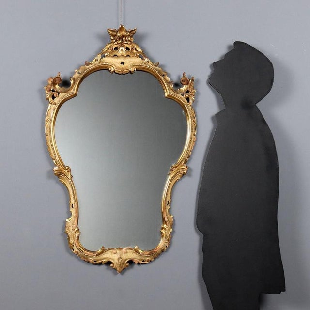 Barocchetto style mirror crafted from carved, lacquered, and gilded wood, featuring a dynamic frame with scrolls and...
