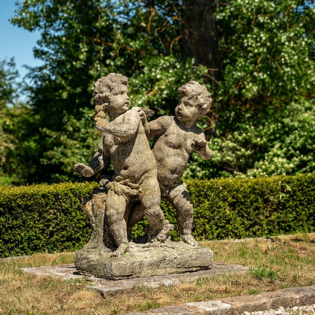 Stone Cast statue of two playing putti with wings and patinated surface.