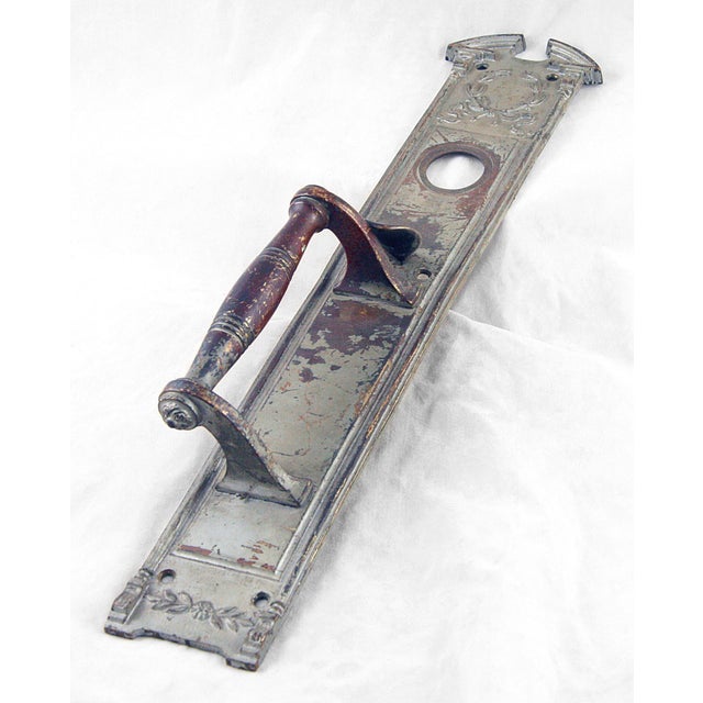 Nickel plated bronze Colonial style door pull with a thumb latch and lock insert. Features a wreath design at the top. The...