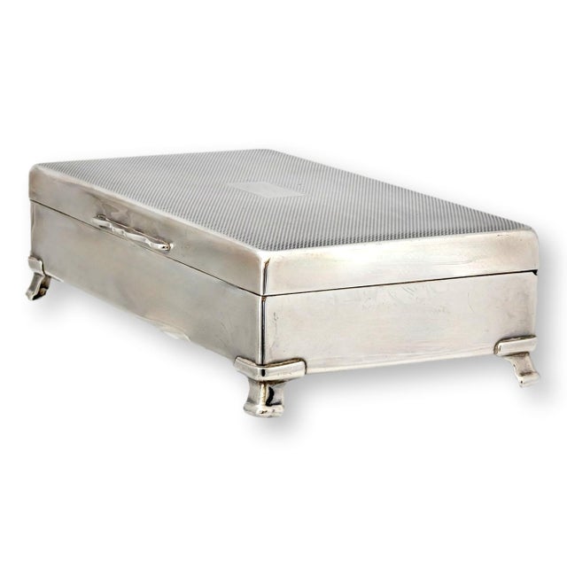 Elegant mid-20th century silverplate cigarette box with a fine engine-turned lid, resting on raised bracket feet. Original...