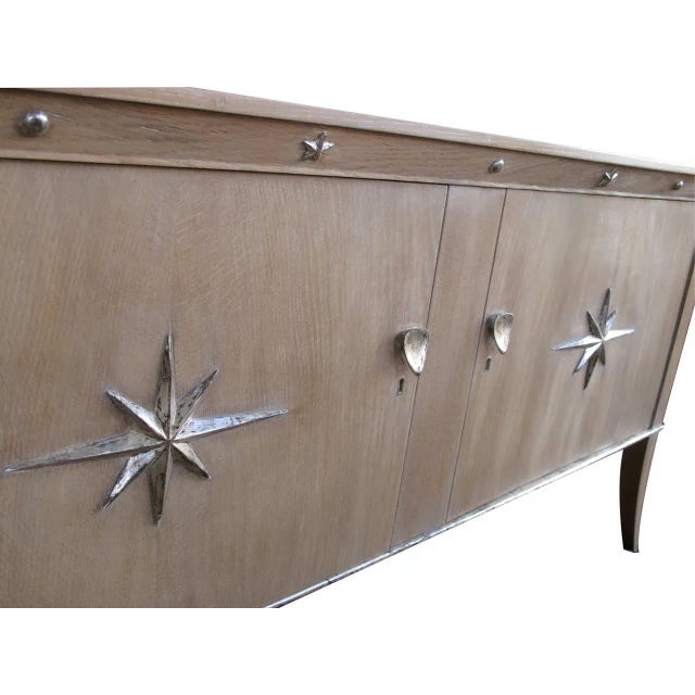 A stylish French mid-century two-door cerused oak sideboard with silver-leaf star relief motifs; the solid cabinet with...