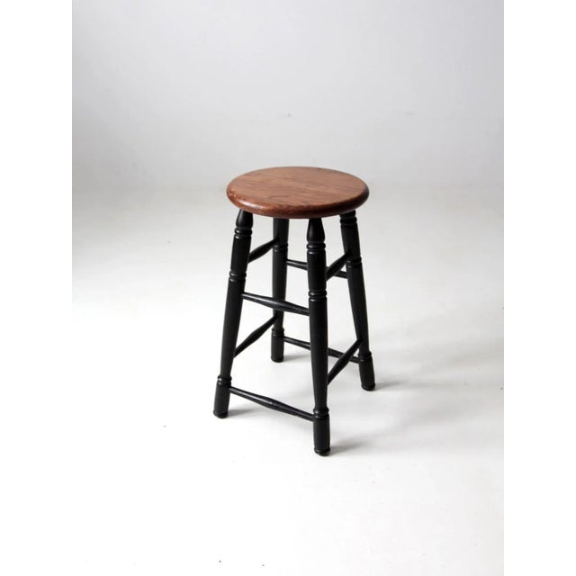This is a vintage wooden stool. It features black turned legs with a round wood seat.
