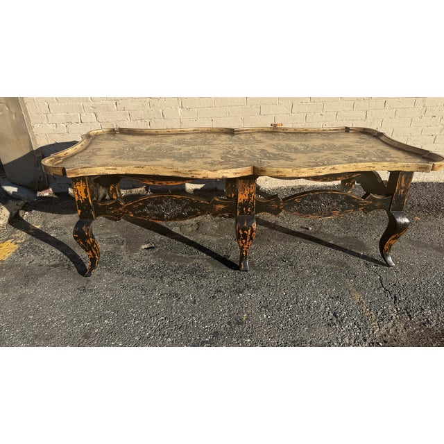 A striking Italian-style tole coffee table featuring a scalloped gilt tray top with pastoral toile motifs in black over a...