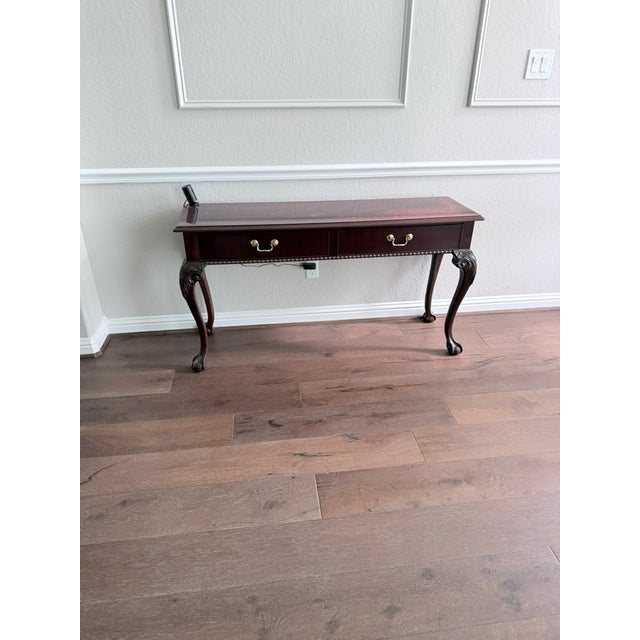 Queen Anne-style dark mahogany console table featuring two brass bail-handle drawers and graceful cabriole legs ending in...