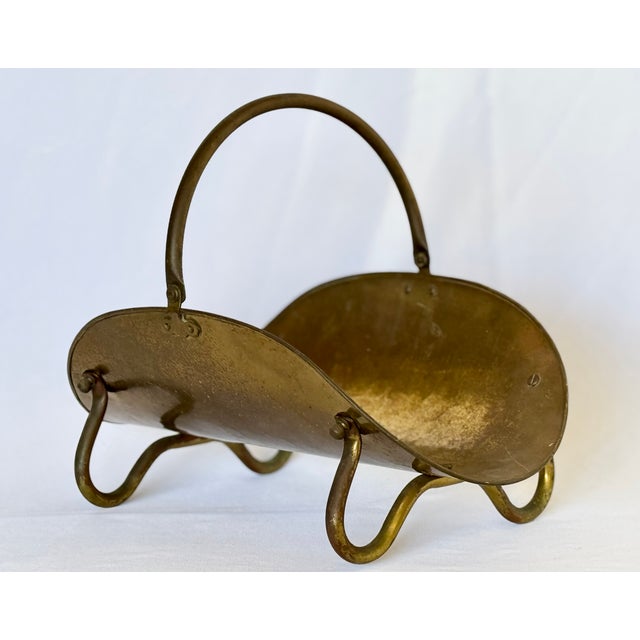 A brass plated copper firewood holder. The curved form accented by a swing loop handle and bent tubular feet. The brass...