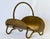 A brass plated copper firewood holder. The curved form accented by a swing loop handle and bent tubular feet. The brass...