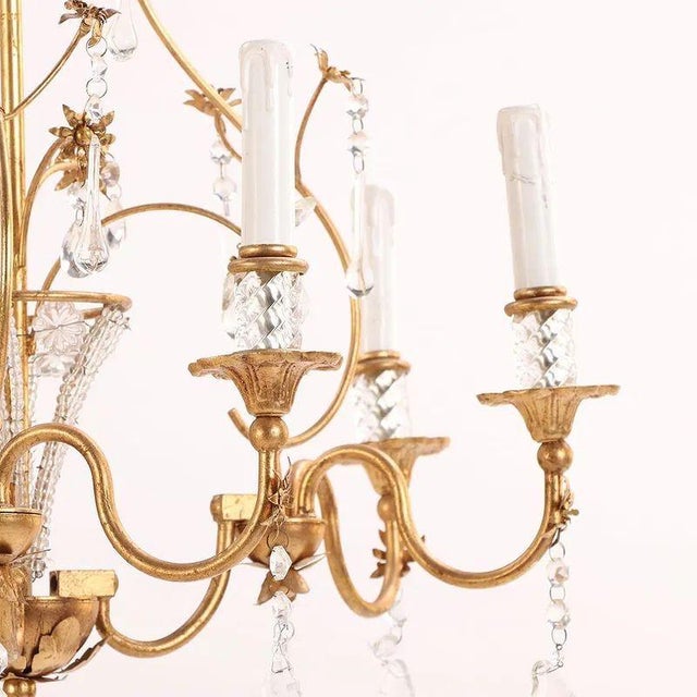 This Vintage French Bagues Manner Gilt Iron and Crystal Chandelier is a luxurious and elegant lighting fixture. The...