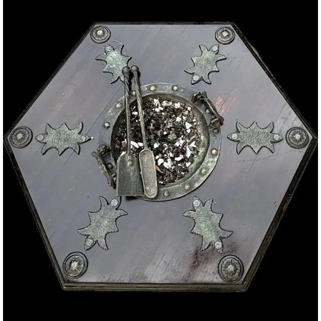 A striking hexagonal coffee table featuring a central brazier bowl with crushed glass and matching metal tools. The richly...