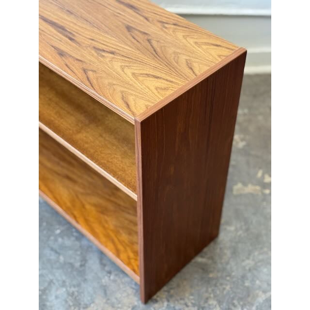 This 1970s low bookcase is made of a warm teak veneer that highlights a natural wood grain pattern across the top and side...