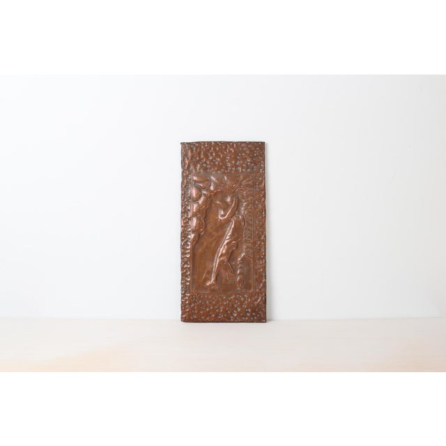 A hand-worked copper repoussé wall plaque depicting a relaxed figure in a sombrero leaning against a wall. Sculpted relief...