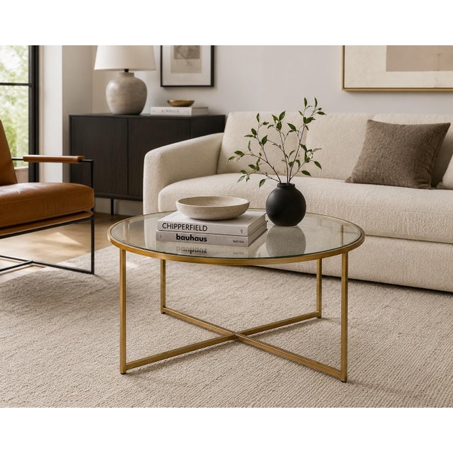 A sleek vintage round coffee table featuring a sunlit brass geometric metal frame and clear glass top. Clean-lined, airy,...