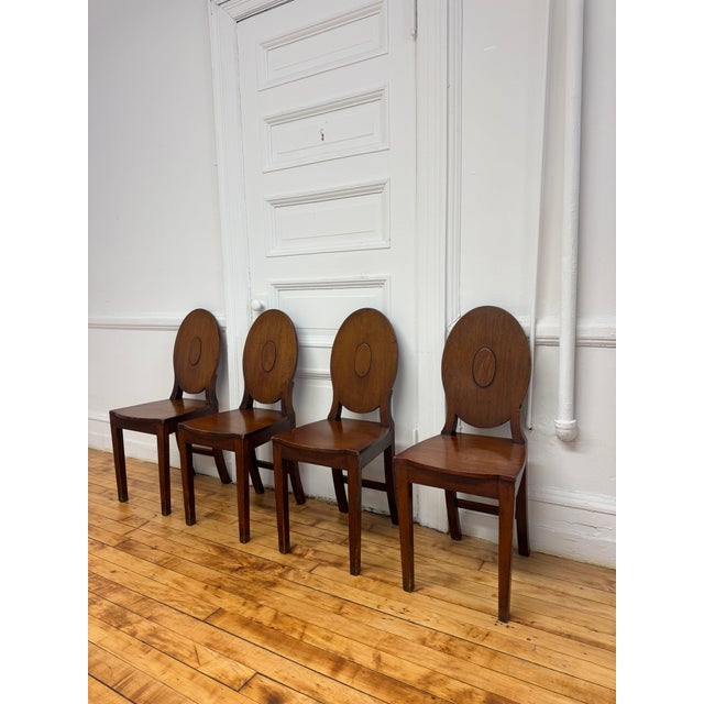 A set of four 18th century English George III hall chairs in solid mahogany that has a warm, even tone with visible wear...