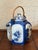 A blue and white Japanese landscape tea pot hand decorated with trees and boats. Handle is made of rattan wrapped metal....