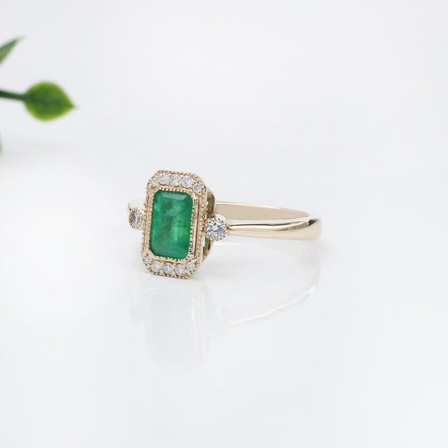 This elegant ring features a 1.07 carat emerald cut Emerald gemstone, beautifully encircled by a halo of shimmering...