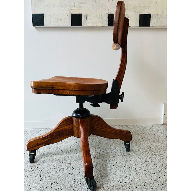 A beautifully restored vintage wooden stenographer chair featuring sculpted solid oak construction, adjustable seating,...
